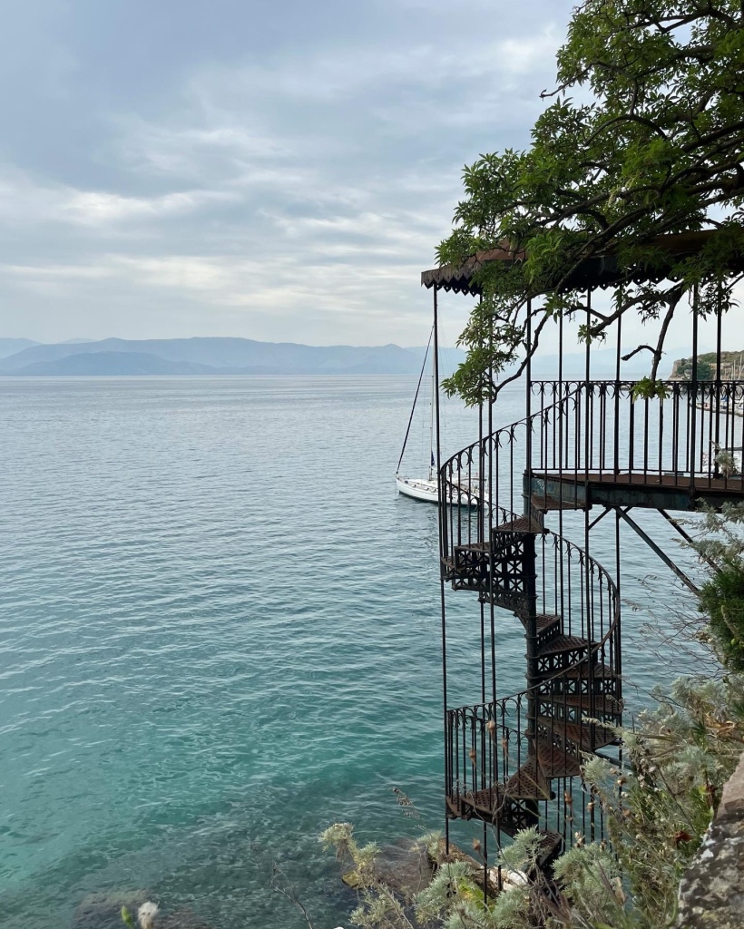 A beautiful metal spiral staircase leads down to turquoise sea in Corfu, Greece. 
